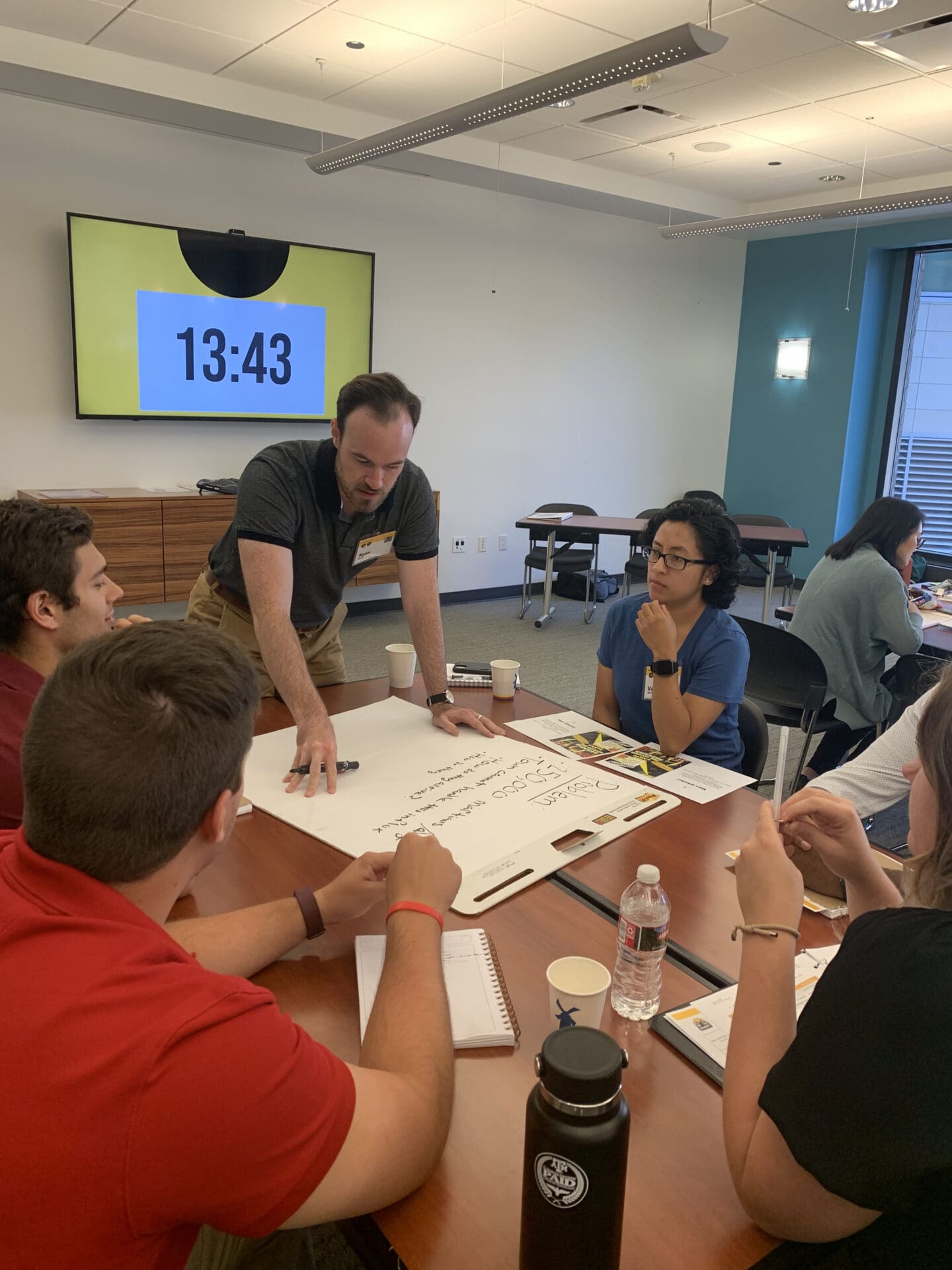 A group of six people sitting around a table writing on a giant notepad.