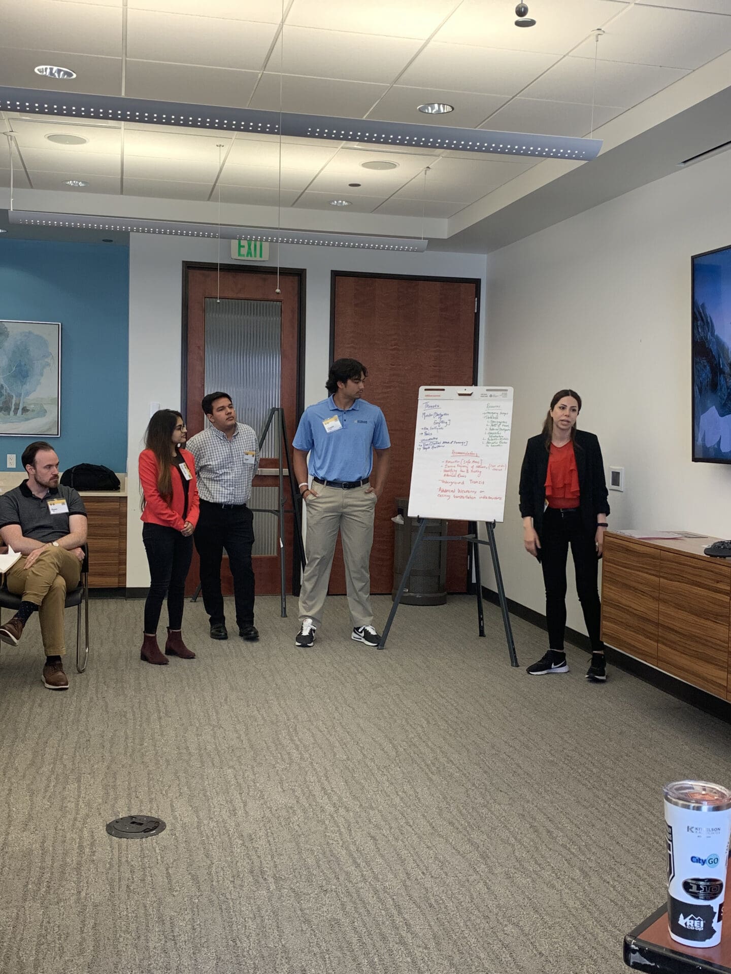 A group of four people standing next to a big notepad presenting.