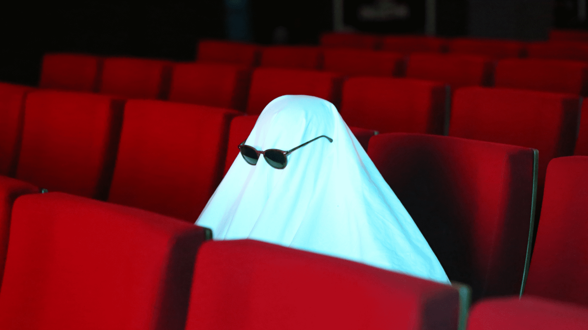 Sheet ghost sitting in red movie theater seats