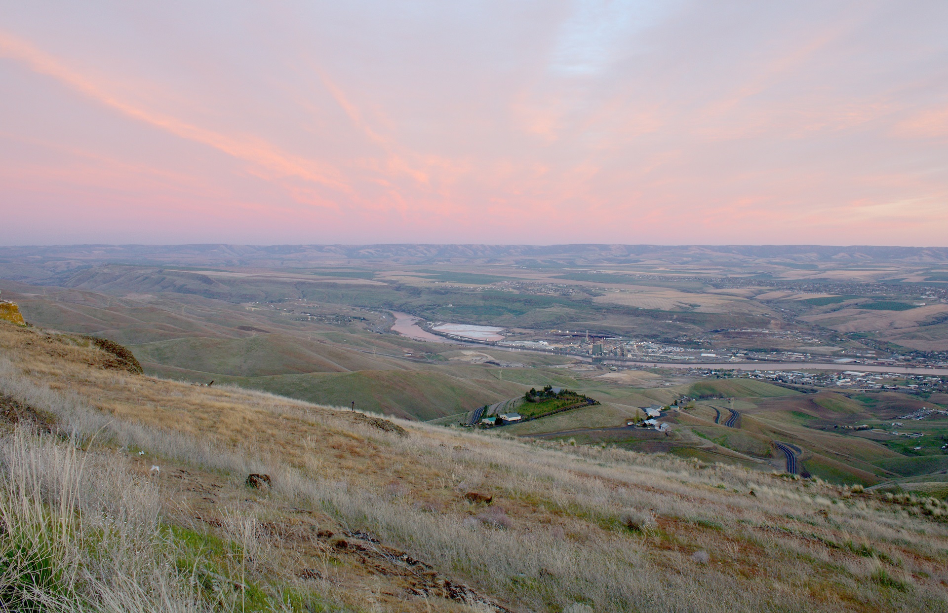 overlook of small town with pink sky at sunset with river and bridge