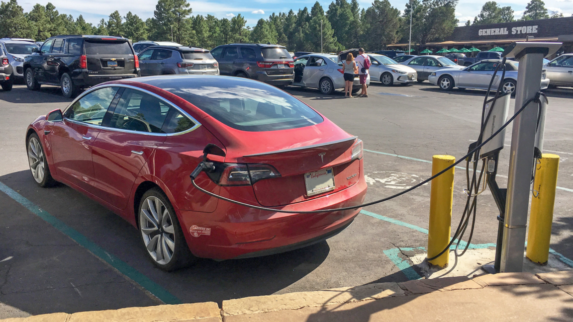 Red car plugged into an EV charge in a parking lot.